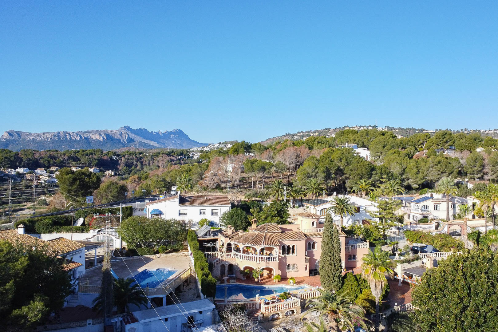 Vue aérienne de la villa méditerranéenne avec piscine privée, terrasses à arcades et jardins arborés offrant un panorama sur les montagnes environnantes.