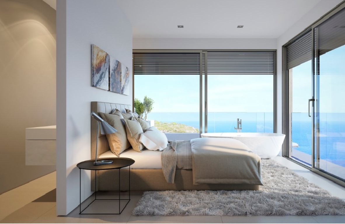 Chambre principale avec baignoire îlot devant de grandes baies vitrées, offrant une vue panoramique sur la mer et un design épuré.
