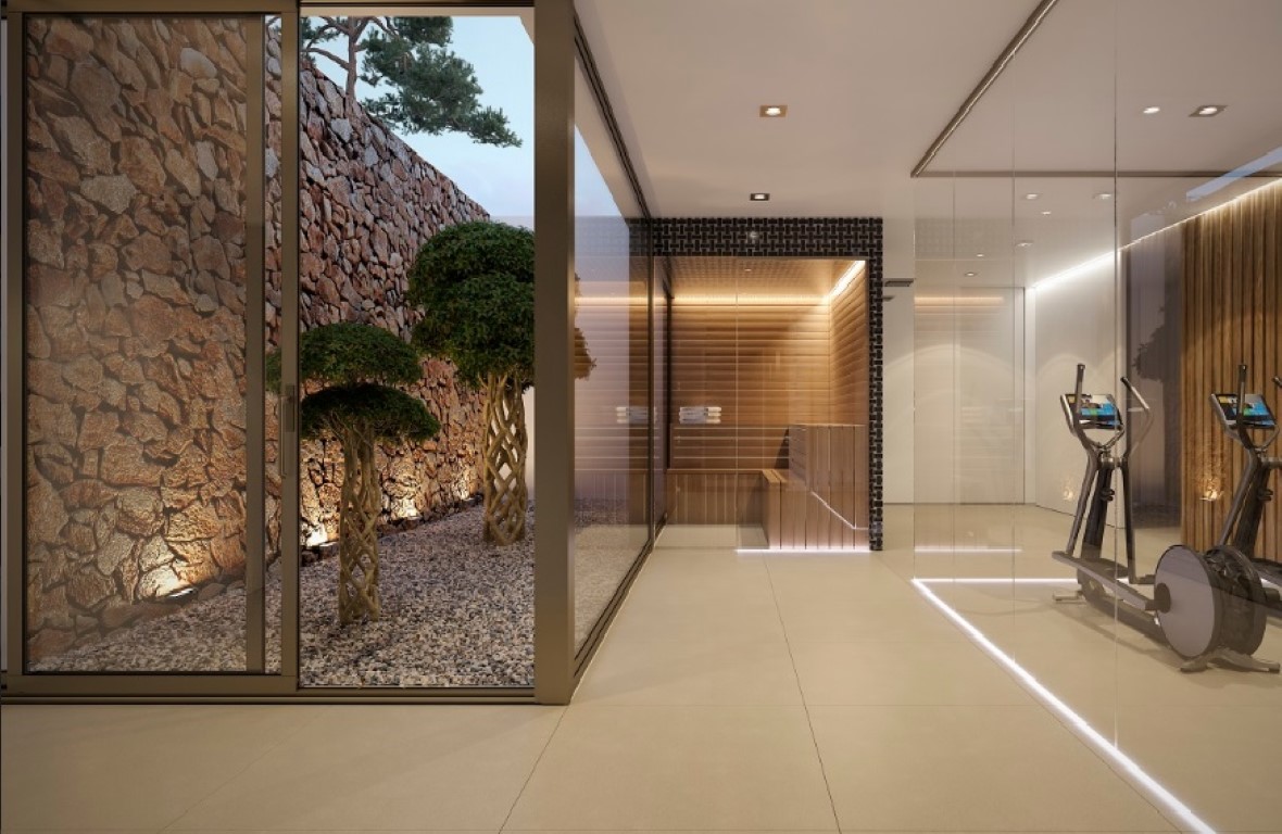 Espace bien-être avec salle de sport vitrée et sauna en bois, ouvert sur un patio extérieur avec mur en pierre naturelle et arbres décoratifs.