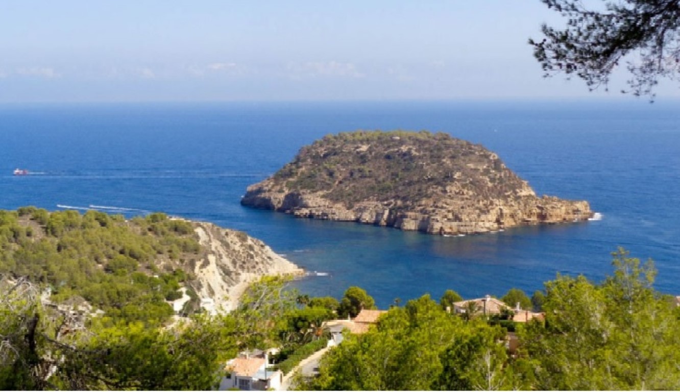 Vues panoramiques sur la mer Méditerranée et l'île de Portitxol, entourées de pins et d'une végétation côtière dense.