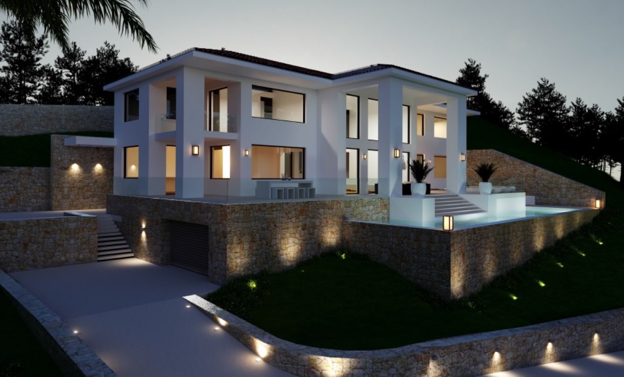 Vue extérieure crépusculaire de la villa avec façade blanche, murs en pierre naturelle, piscine éclairée et accès au garage au niveau inférieur.