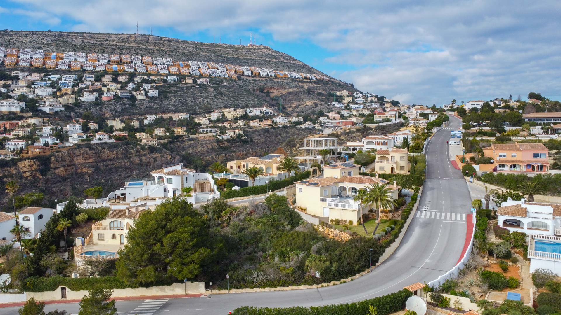 Vue aérienne du quartier résidentiel de Cumbre del Sol, mettant en avant la route sinueuse, les villas méditerranéennes et les habitations en terrasses sur la colline.