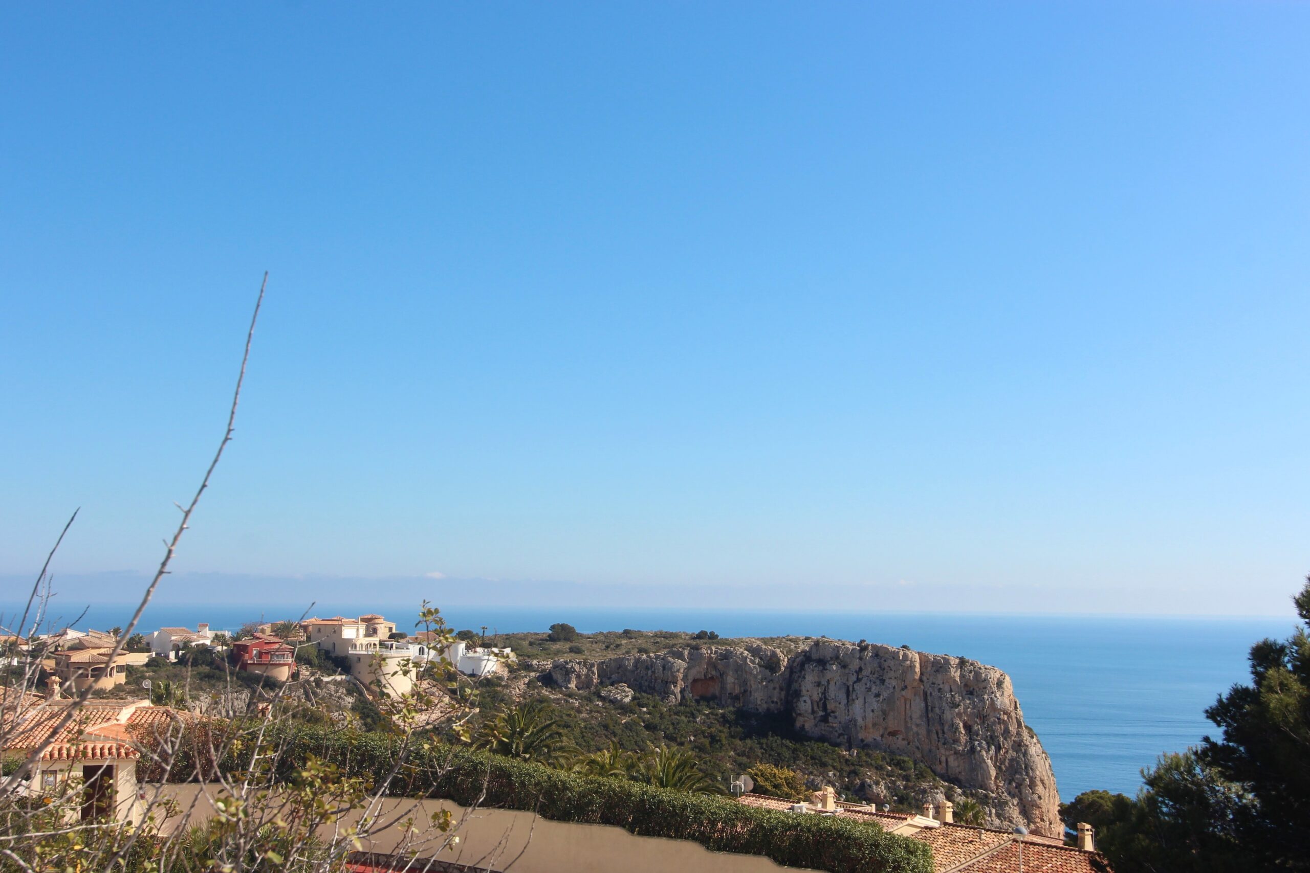 Vue panoramique depuis la propriété sur la mer Méditerranée et les falaises escarpées, avec des toits en terre cuite et une végétation côtière sous un ciel azur.