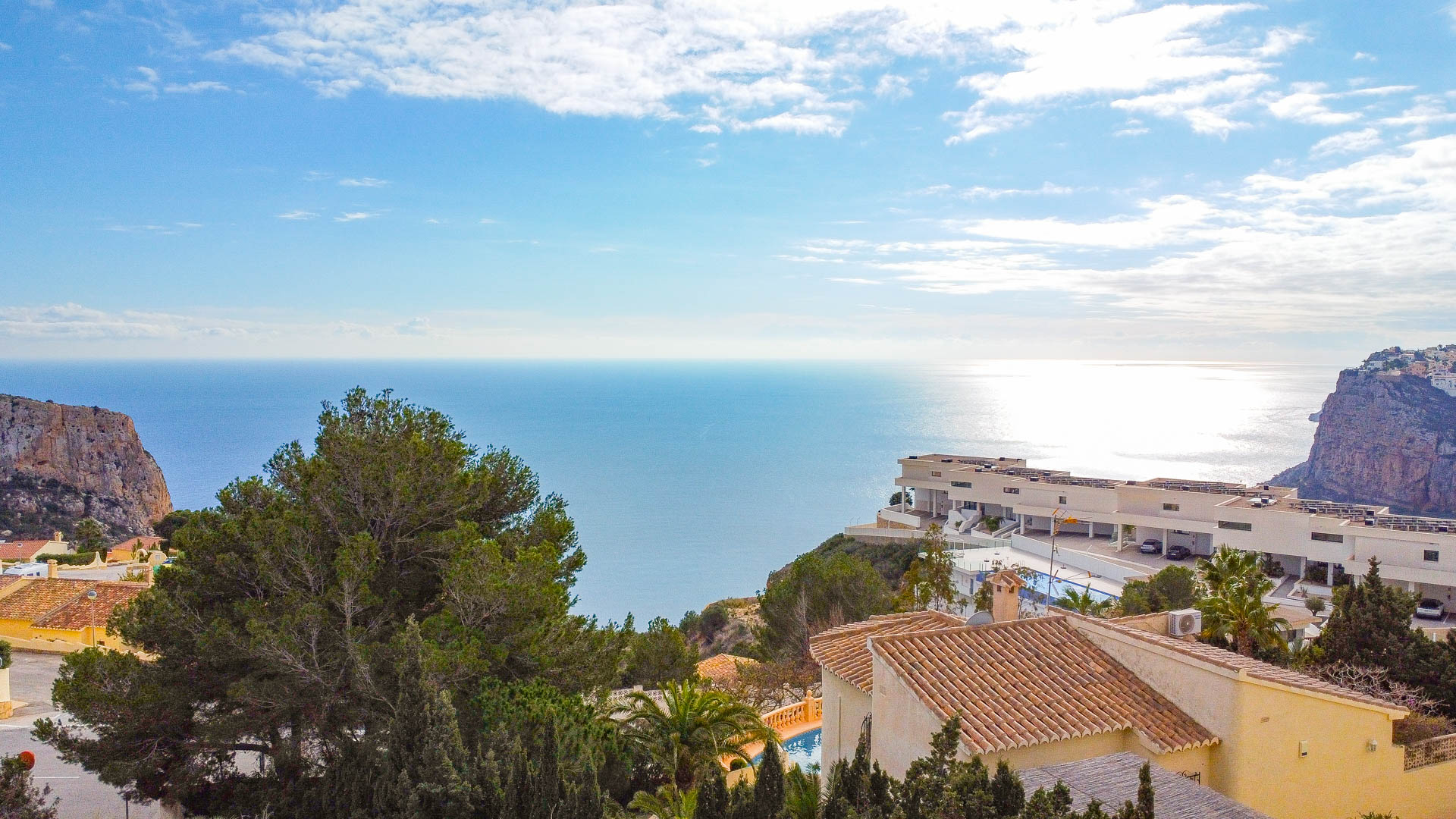 Vue panoramique sur la mer Méditerranée depuis Cumbre del Sol, mettant en valeur les falaises côtières, l'architecture variée et la végétation de pins environnante.
