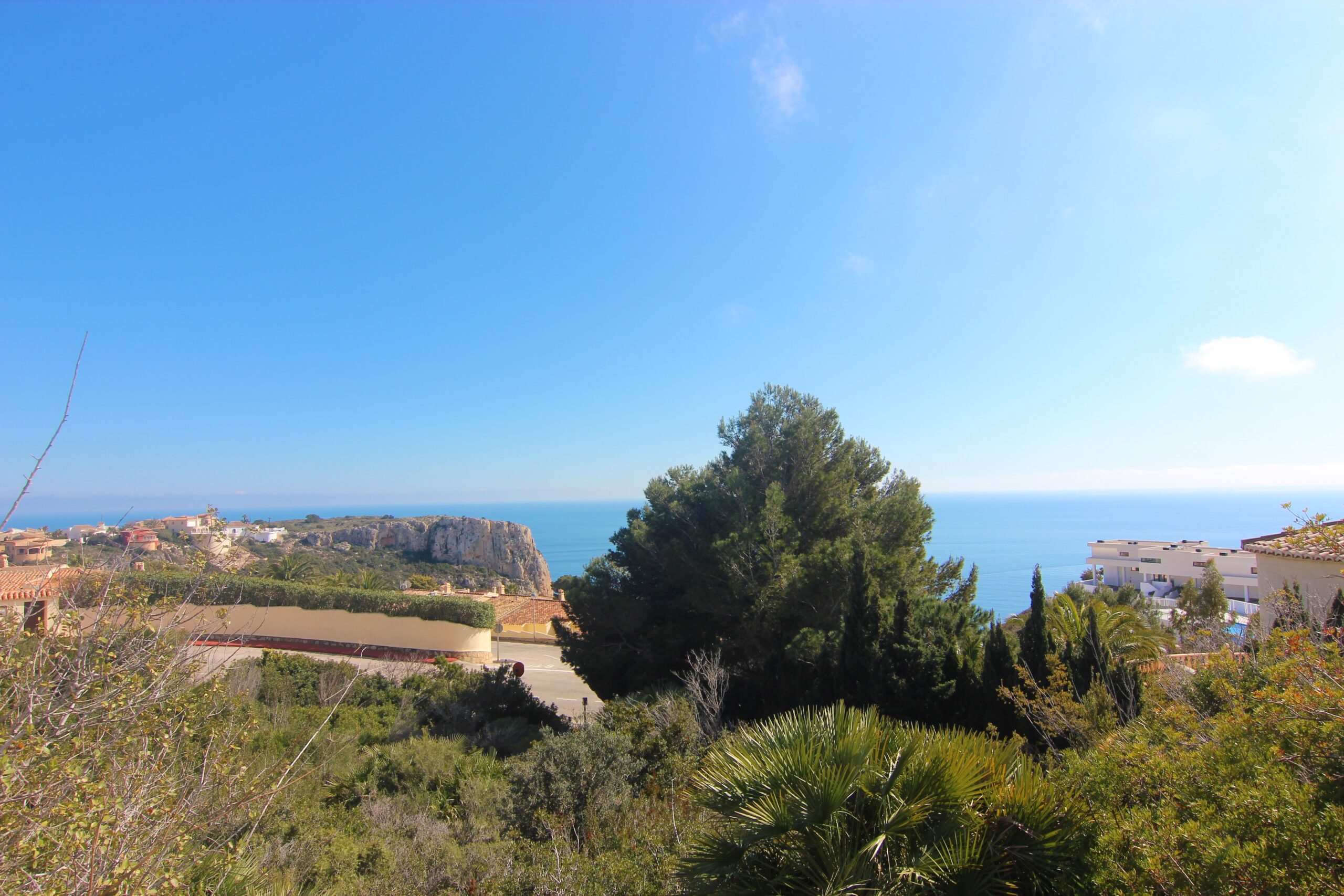 Vue panoramique sur la mer Méditerranée et les falaises de Cumbre del Sol depuis une position surélevée entourée de végétation locale et de pins.