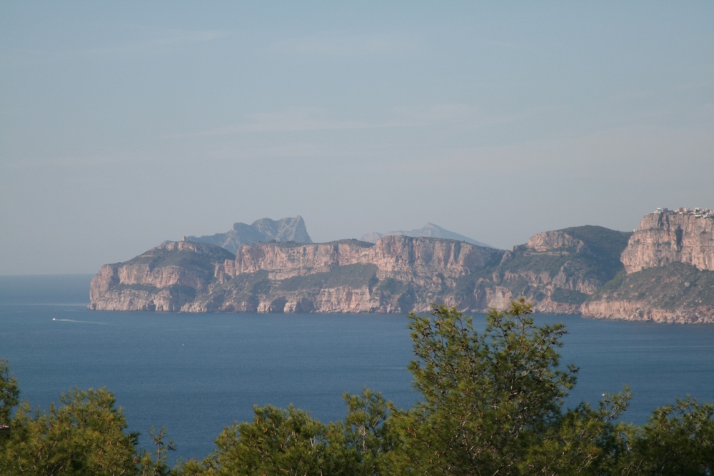 Vue panoramique sur la mer Méditerranée et les falaises escarpées de Javea, encadrée par des pins indigènes sous un ciel dégagé.