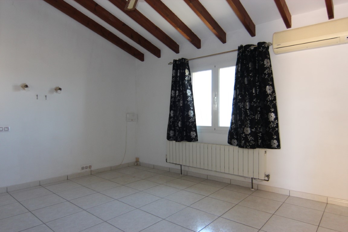 Pièce mansardée avec poutres apparentes en bois sombre, sol en carrelage clair, radiateur mural et unité de climatisation individuelle.