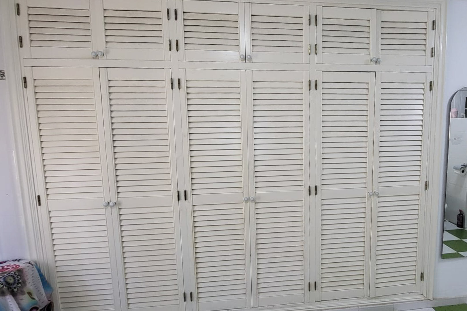 Armoire en bois intégrée avec portes à persiennes et boutons ronds, couvrant tout le mur.