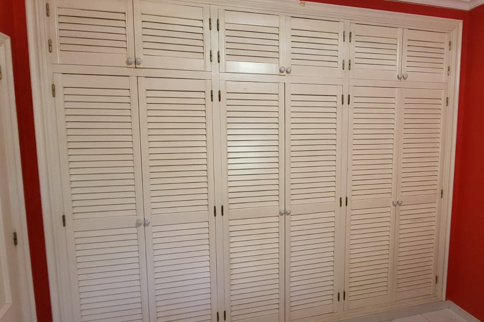 Armoire intégrée avec portes persiennes dans une chambre avec mur rouge.