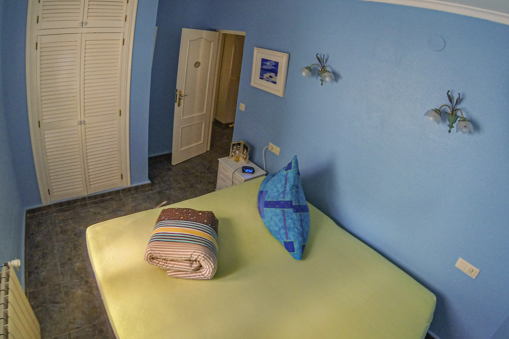 Chambre aux murs bleus, armoire intégrée en bois blanc et linge de lit plié.