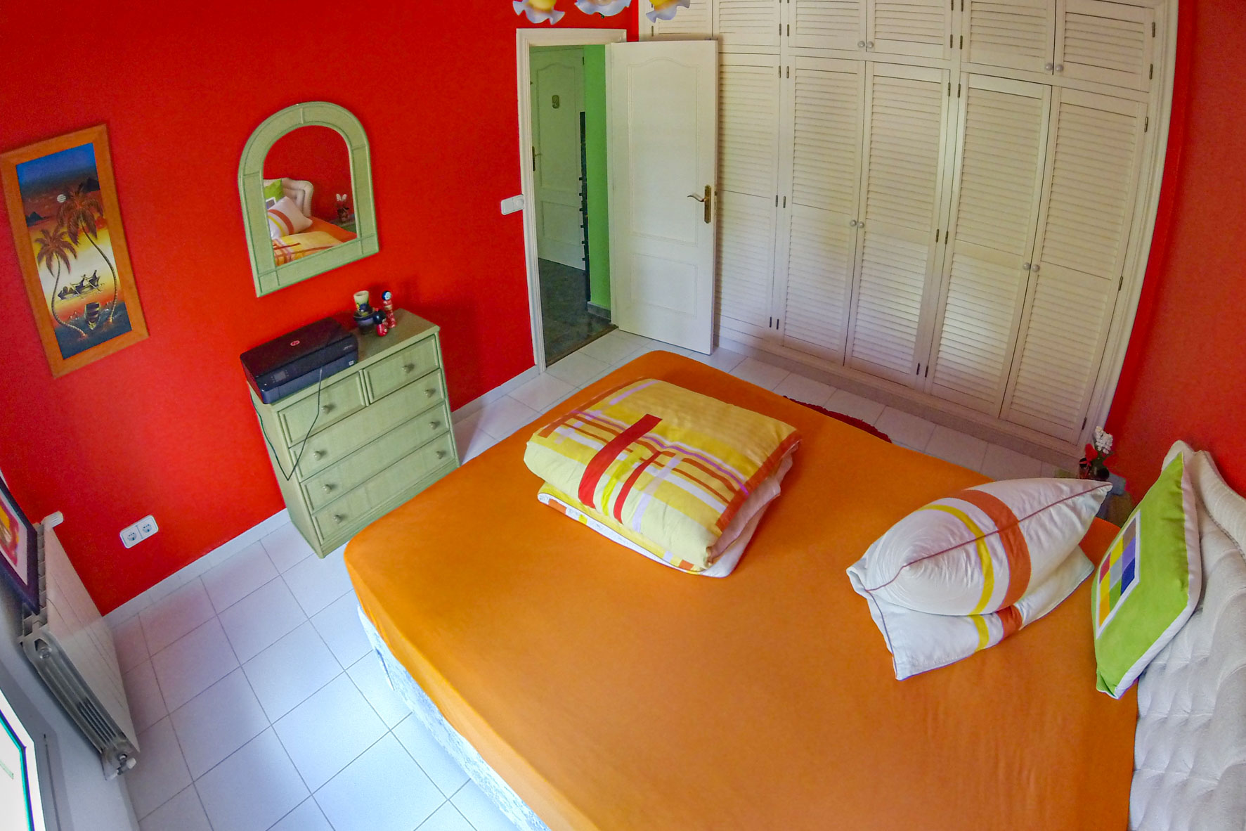 Chambre avec murs rouges, placard intégré blanc et lit avec literie orange.