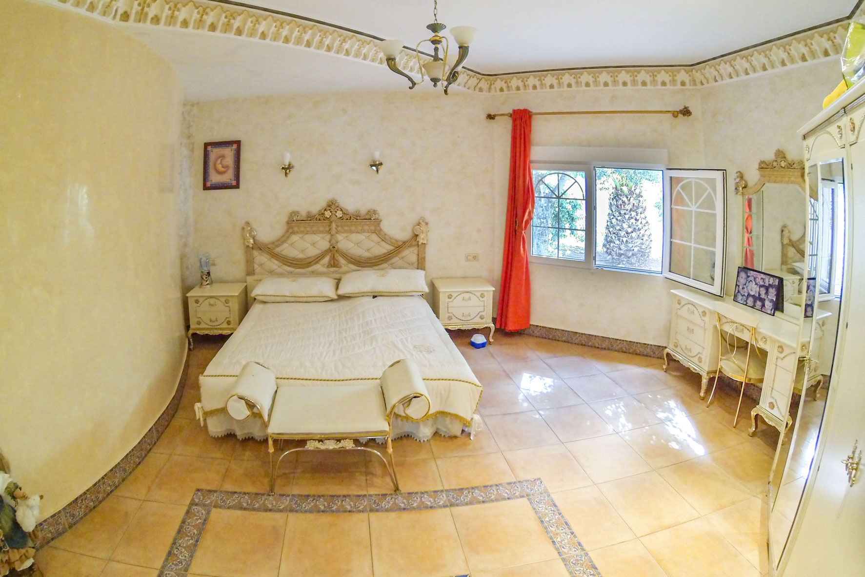 Chambre principale meublée avec lit double, coiffeuse et vue sur le jardin par une fenêtre.