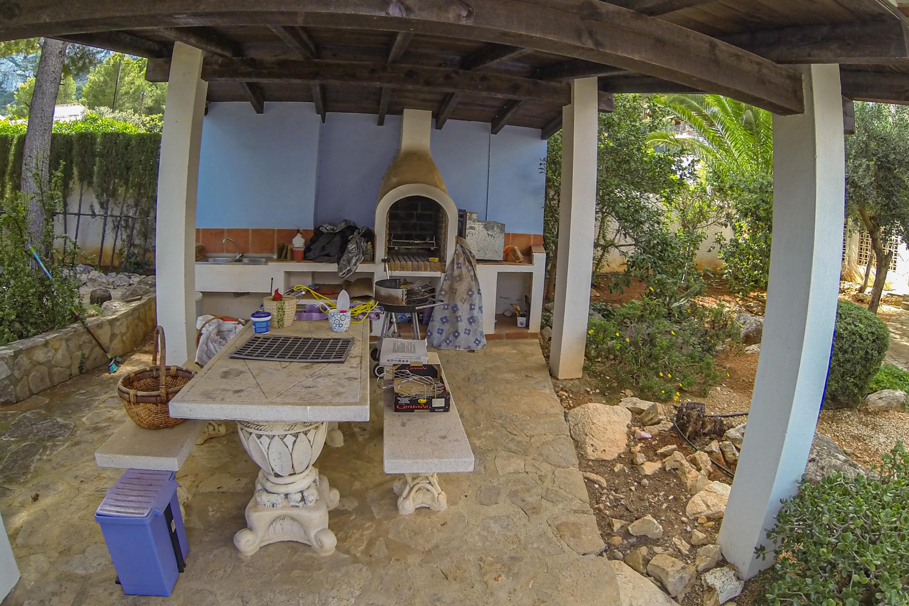 Espace barbecue couvert avec four en brique et table en pierre, niché dans un jardin luxuriant.