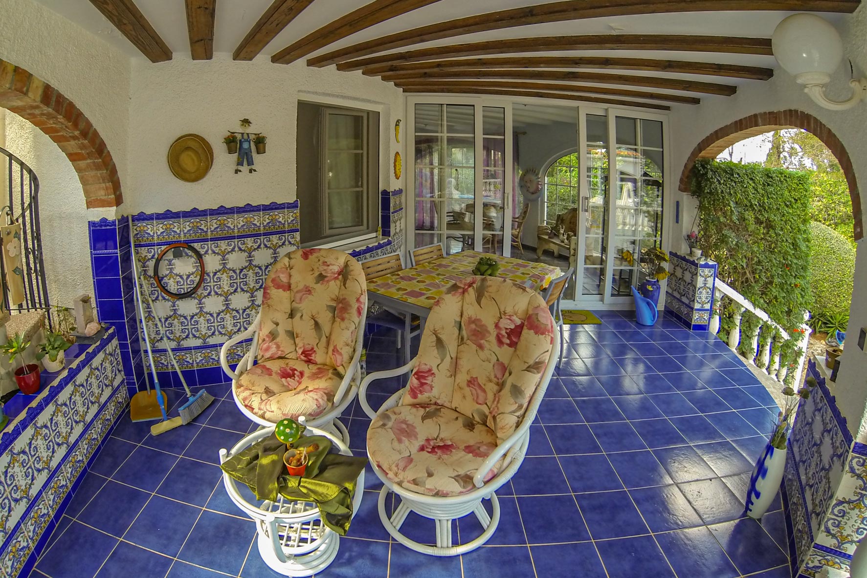 Porche couvert avec carrelage bleu, arches en brique et chaises fleuries.