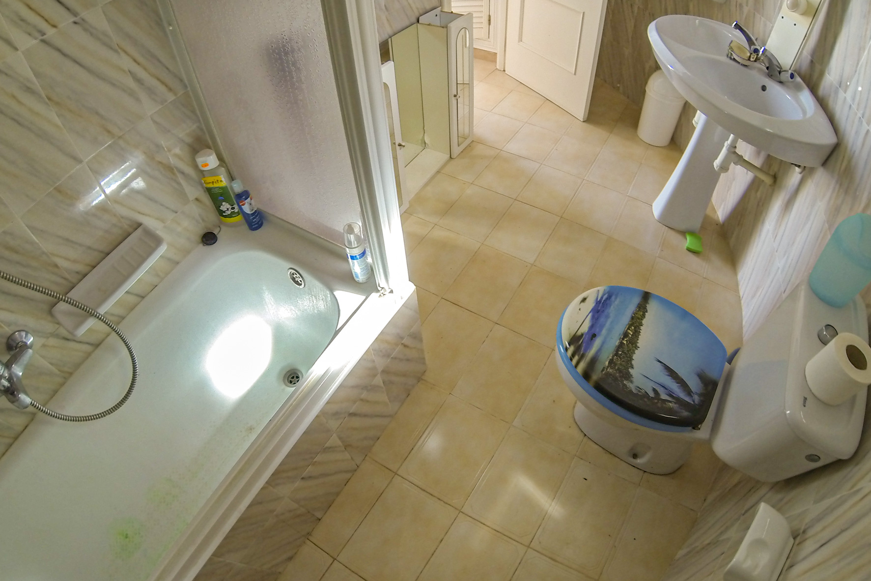 Salle de bain avec baignoire, lavabo sur pied et toilettes avec couvercle décoré.