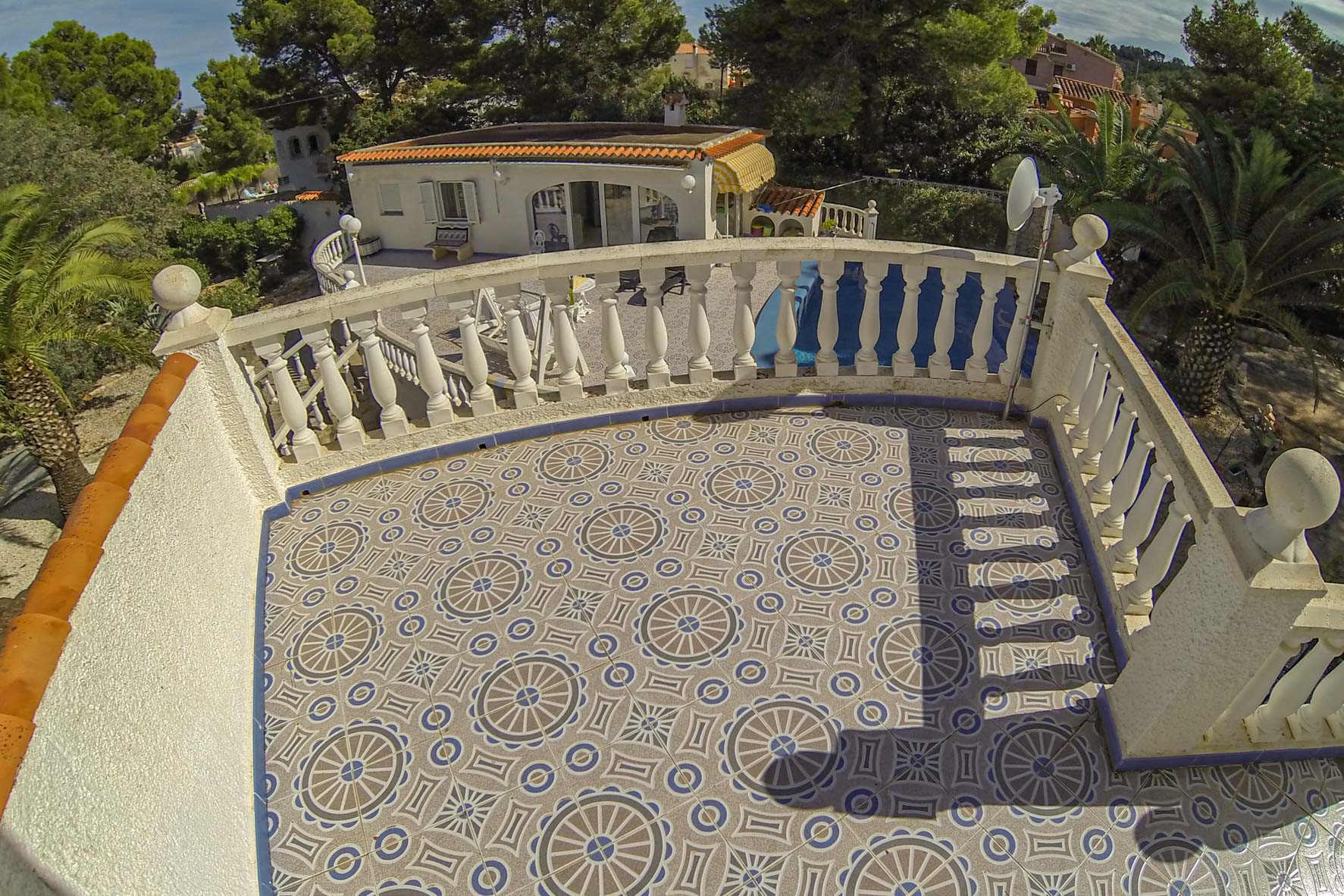 Terrasse avec carrelage à motifs et rambarde blanche donnant sur la propriété et la verdure.