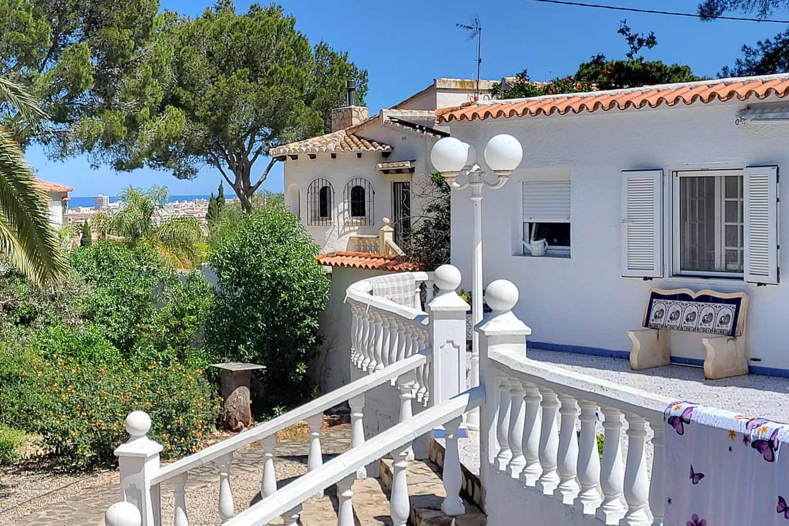 Vue extérieure de la villa avec une balustrade blanche, des jardins et une vue lointaine sur la ville.