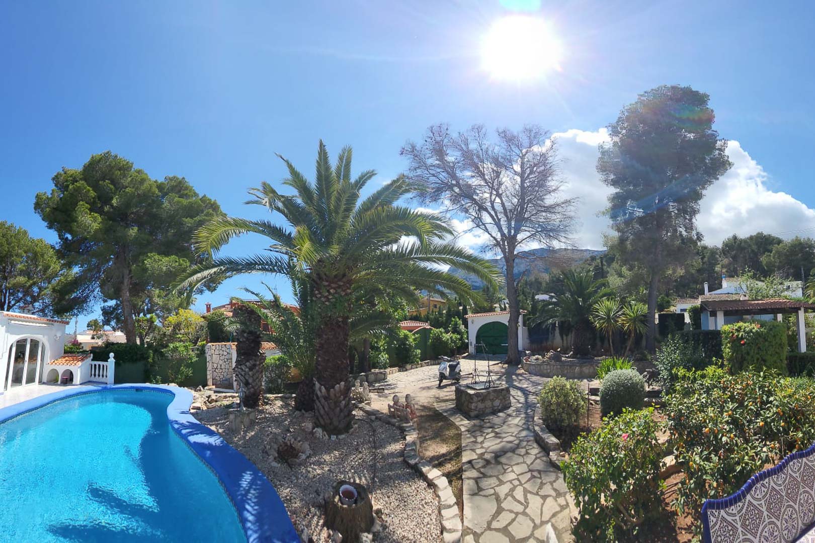 Vue sur la piscine bleu turquoise et les jardins avec palmiers et chemin de pierre à Denia.