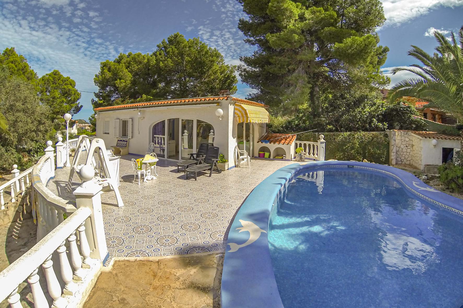 Vue sur la piscine privée avec mosaïque bleue et le pool house avec store jaune.