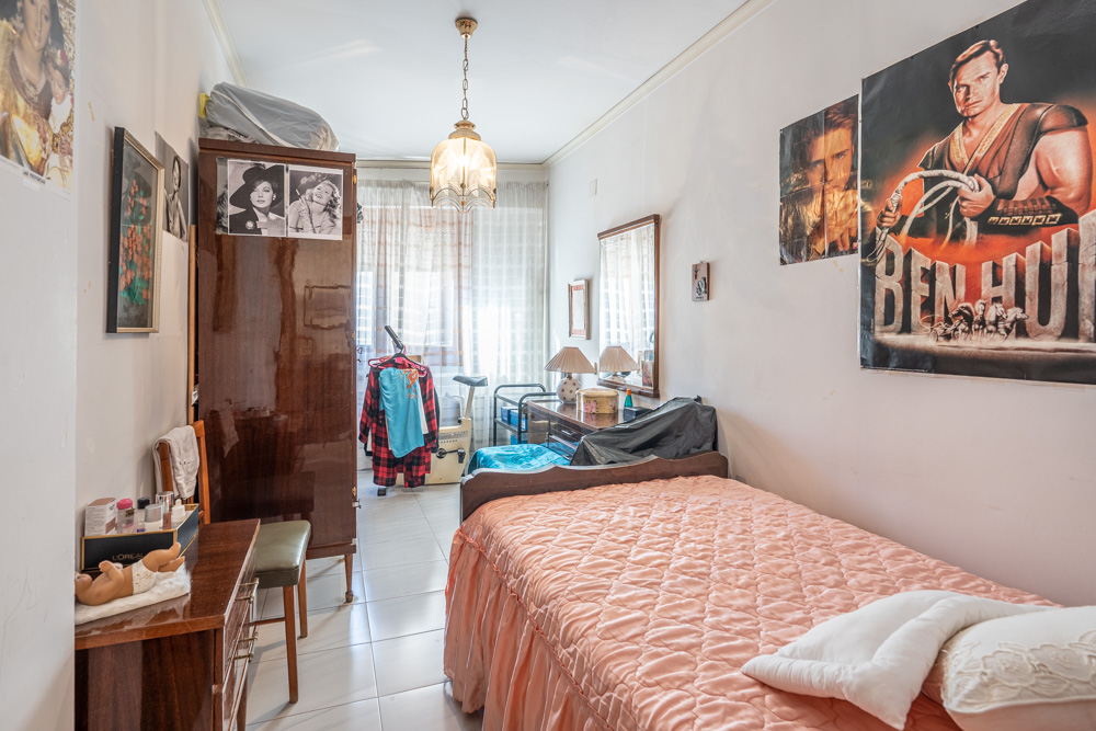 Chambre individuelle avec armoire en bois sombre, bureau et sol en carrelage clair. La pièce dispose d'une fenêtre apportant une luminosité naturelle constante.
