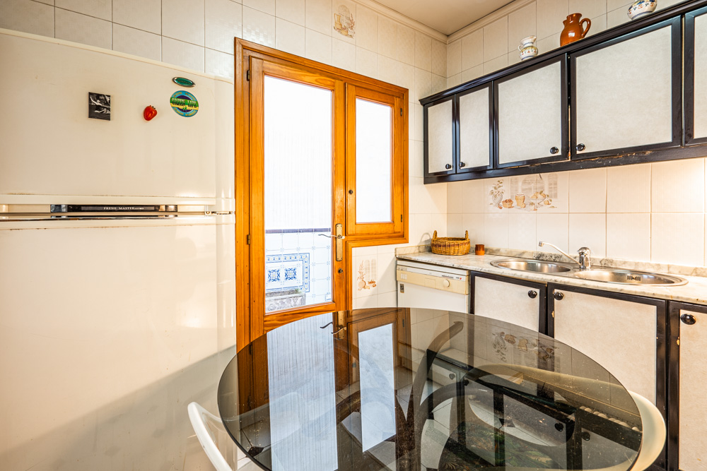 Cuisine fonctionnelle avec placards à bordure sombre, plan de travail en marbre et porte vitrée en bois menant au patio. Comprend une table à manger ronde en verre.