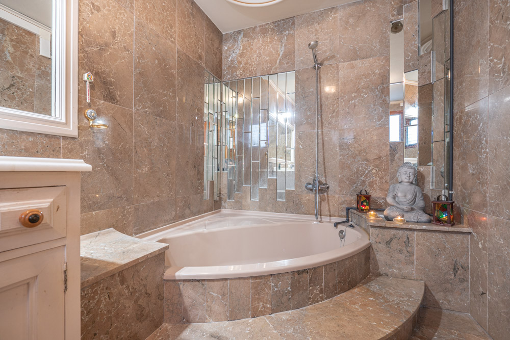 Salle de bain élégante avec baignoire d'angle encastrée, murs en marbre poli et un agencement original de miroirs verticaux.