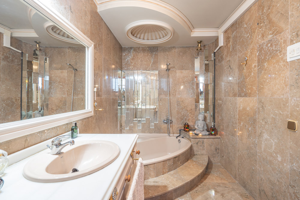 Salle de bain luxueuse en marbre avec baignoire encastrée, meuble vasque blanc et un élément de plafond circulaire décoratif.