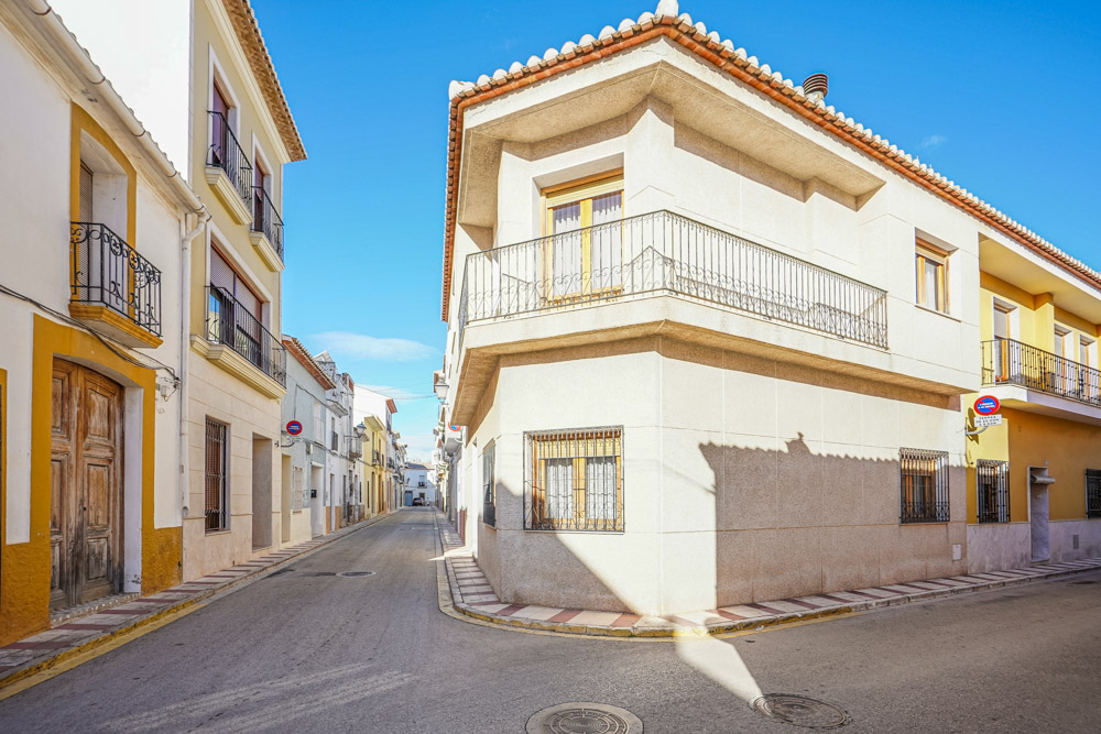 Vue extérieure de cette maison de ville en angle, avec sa façade claire, son balcon filant en fer forgé et sa situation privilégiée dans une ruelle calme du village.