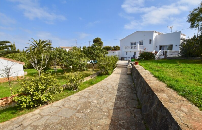 Allée en pierre naturelle traversant le jardin méditerranéen vers la villa blanche, avec des pelouses entretenues, des palmiers et des balustrades classiques.