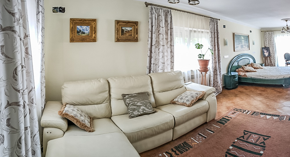 Espace de vie de la maison d'amis comprenant un canapé en cuir crème, un sol en carrelage et un coin nuit intégré avec une décoration de style classique.