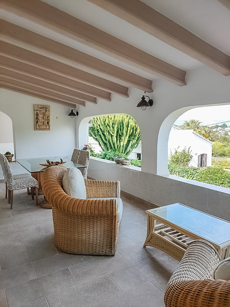 Grande naya couverte avec poutres en bois apparentes, mobilier en osier et arches traditionnelles offrant une vue sur le jardin méditerranéen.