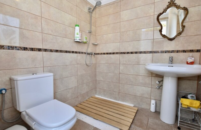 Salle de bain avec douche à l'italienne, caillebotis en bois, carrelage beige à frise décorative et miroir classique au cadre doré.