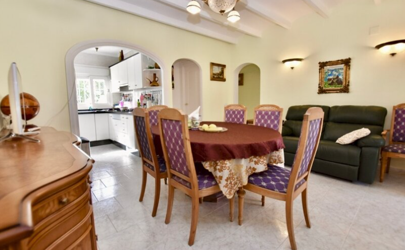 Salon-salle à manger de la maison d'amis avec poutres apparentes, mobilier classique et arche ouvrant sur la cuisine équipée.