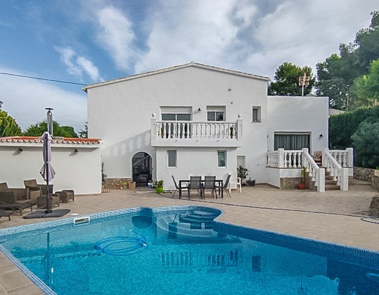 Vue extérieure de la piscine en mosaïque bleue entourée d'une terrasse dallée, avec la façade blanche de la villa et ses balustrades classiques.