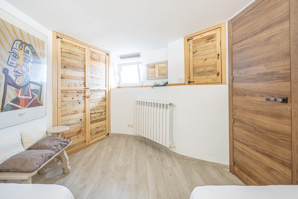 Chambre avec placards intégrés en bois rustique, sol en grès cérame imitation bois, radiateur mural et décoration murale artistique.
