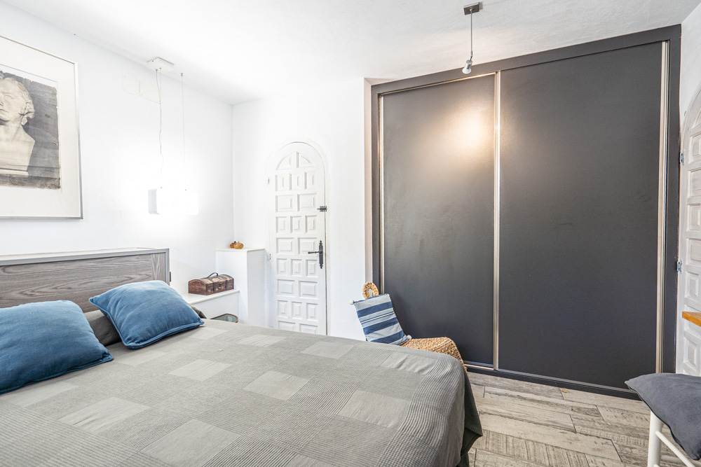 Chambre avec un grand placard intégré aux portes coulissantes sombres, un sol en grès cérame imitation bois et une porte voûtée de style traditionnel.