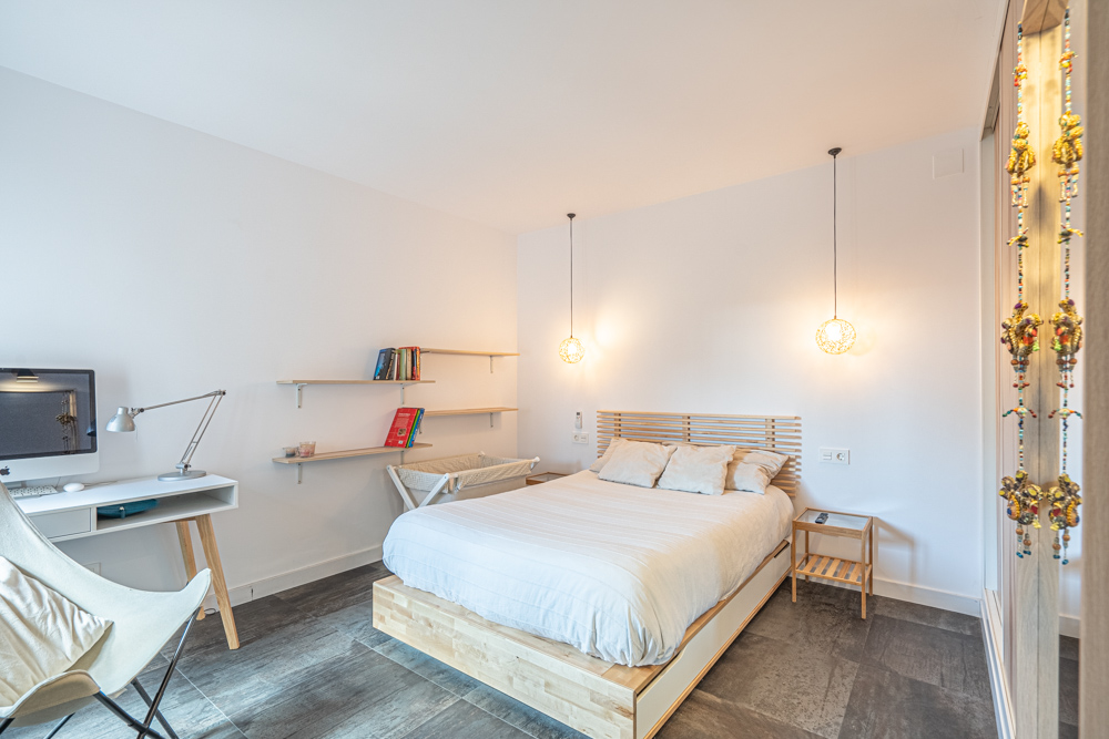 Chambre moderne avec lit en bois, coin bureau intégré et étagères murales. Éclairage suspendu design et sol en grès cérame foncé complètent l'espace.