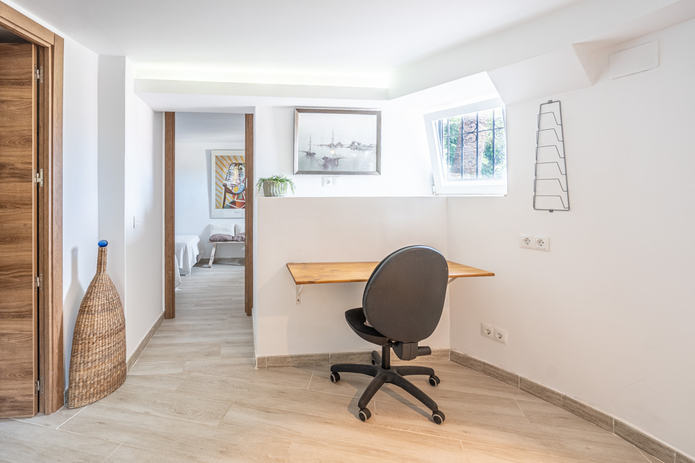 Coin bureau intégré avec bureau en bois, chaise ergonomique et éclairage LED indirect. Sols en grès cérame imitation bois et vue vers les chambres adjacentes.