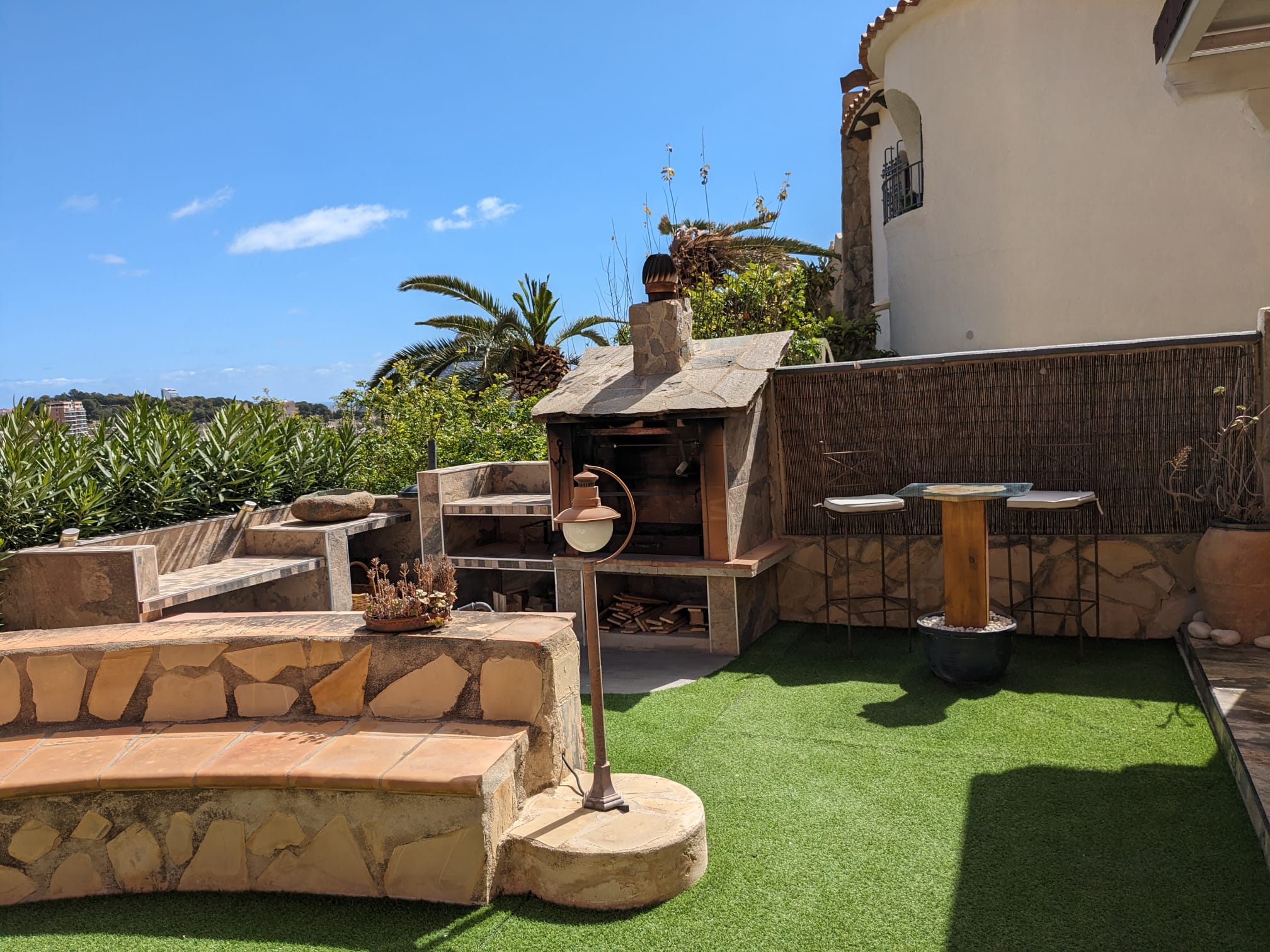 Espace barbecue extérieur en pierre naturelle avec gazon synthétique, bancs maçonnés et un coin bar offrant une vue sur la mer Méditerranée.