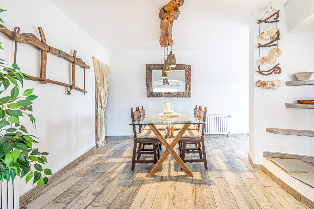 Espace salle à manger rustique avec table en verre et pieds en bois, doté d'un luminaire suspendu en poutre naturelle et d'un grand miroir au cadre en bois massif.