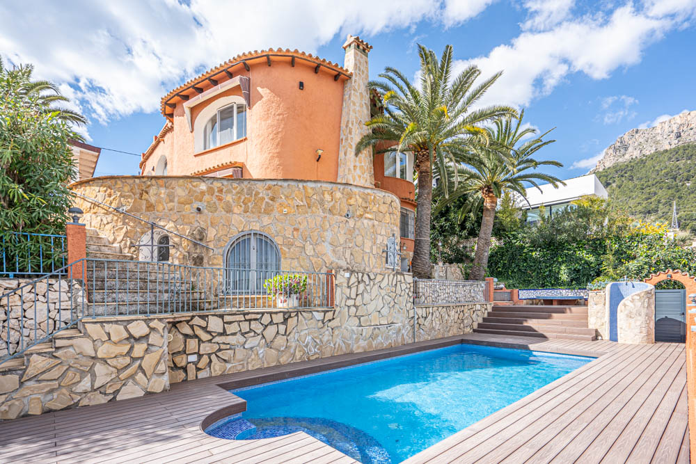 Extérieur de la villa avec piscine privée, terrasse en bois, murs en pierre naturelle et vue dégagée sur les montagnes et les palmiers.