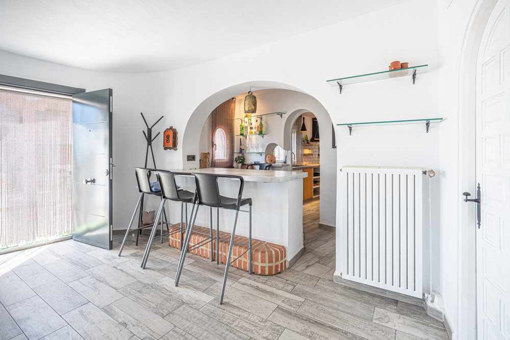 Hall d'entrée avec bar de petit-déjeuner, sol en grès cérame effet bois et une arche élégante ouvrant sur la cuisine équipée.