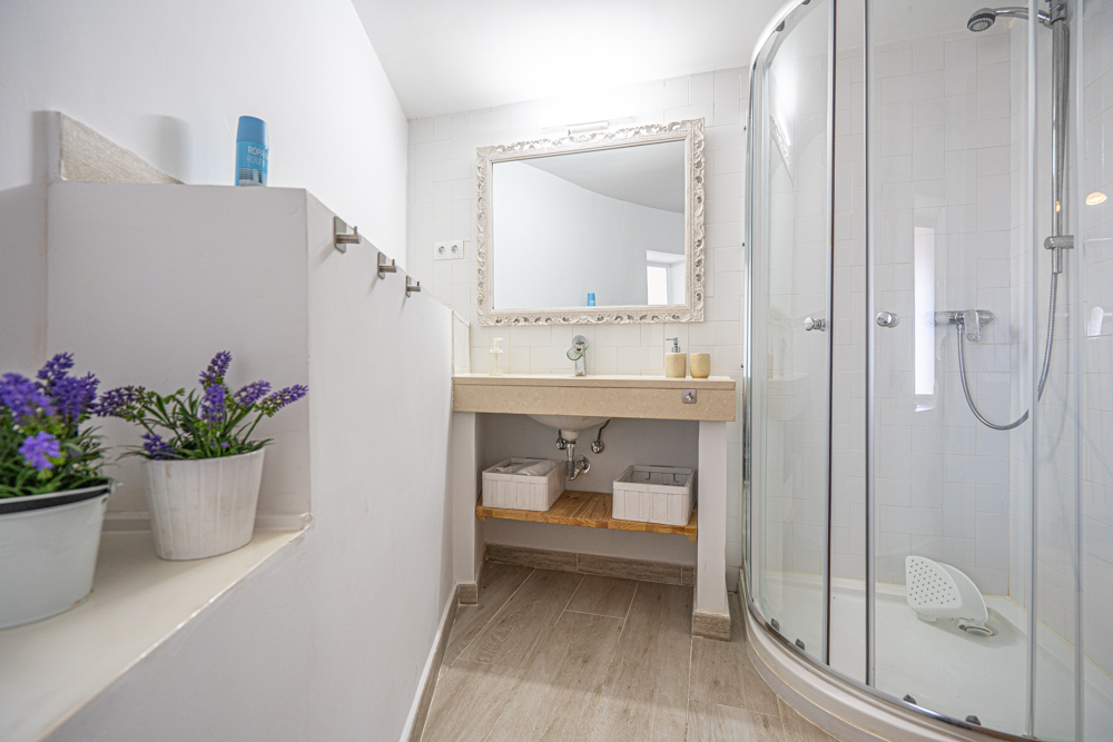 Salle de bain rénovée avec cabine de douche d'angle, vasque sur plan en pierre, miroir à cadre mouluré et sol en grès cérame aspect bois.