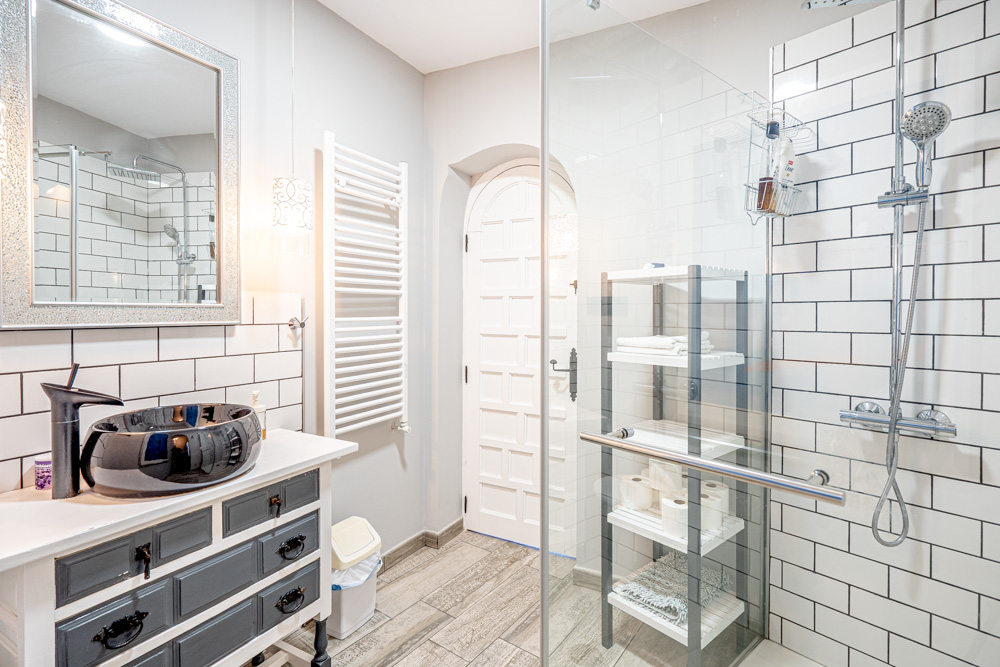 Salle de bain rénovée avec vasque noire sur meuble rustique, douche à l'italienne avec carrelage métro et paroi vitrée.