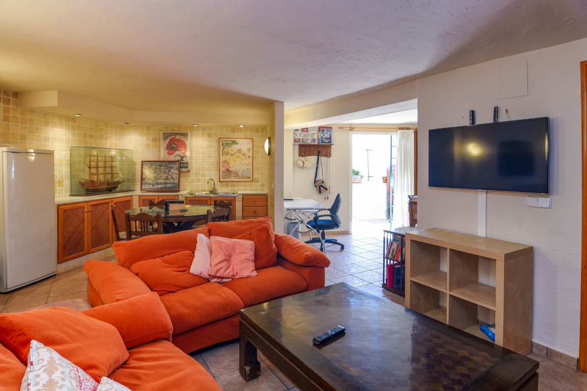 Espace de vie polyvalent avec canapés orange, coin bureau et une kitchenette intégrée avec des finitions en bois et carrelage rustique.