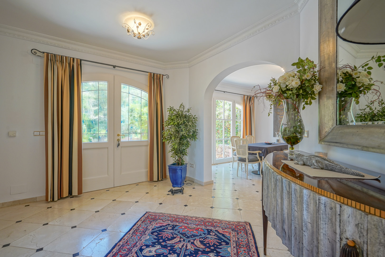 Hall d'entrée élégant avec sol en marbre et cabochons noirs. Une arche s'ouvre sur la salle à manger, mettant en valeur les menuiseries blanches et la lumière naturelle.