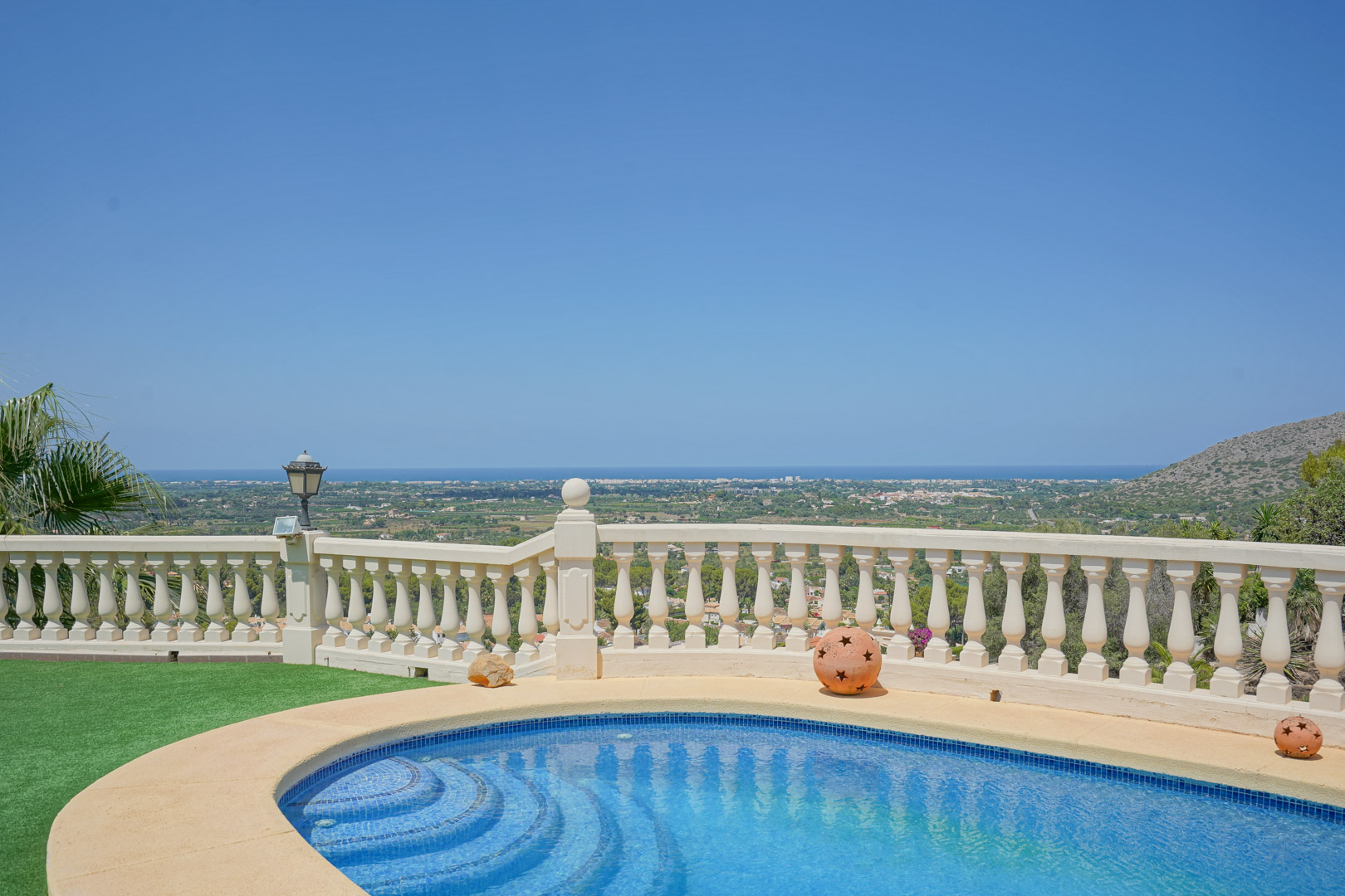 Piscine incurvée avec mosaïque bleue et balustrade classique en pierre, offrant une vue panoramique imprenable sur la vallée et le littoral méditerranéen.