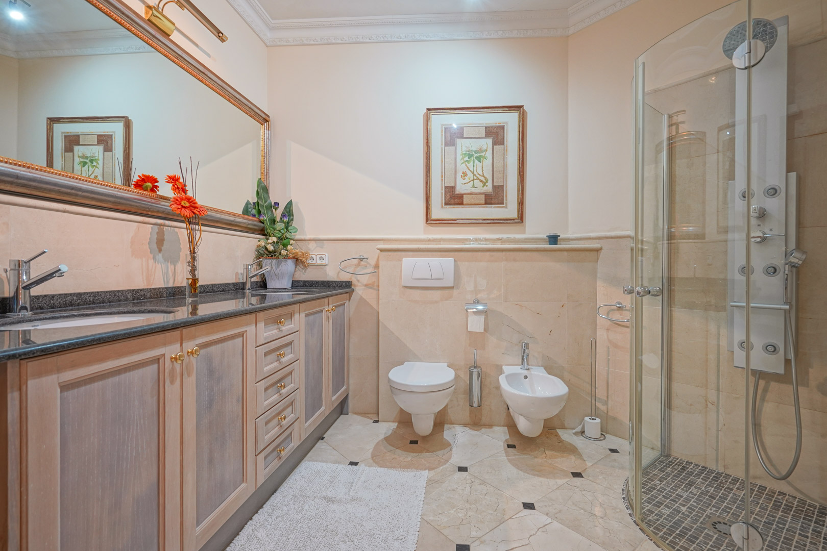 Salle de bain avec double vasque en granit, meubles en bois et une douche vitrée équipée d'une colonne d'hydromassage sur un sol en marbre poli.