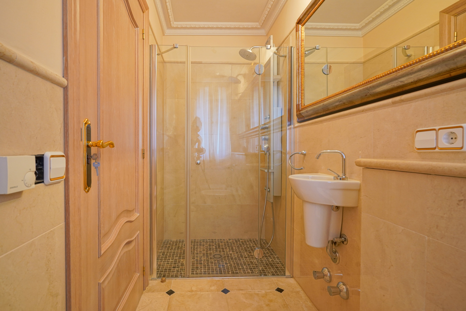 Salle d'eau revêtue de marbre avec douche à l'italienne, sol en mosaïque et paroi vitrée. Comprend un lavabo compact et un miroir au cadre doré.