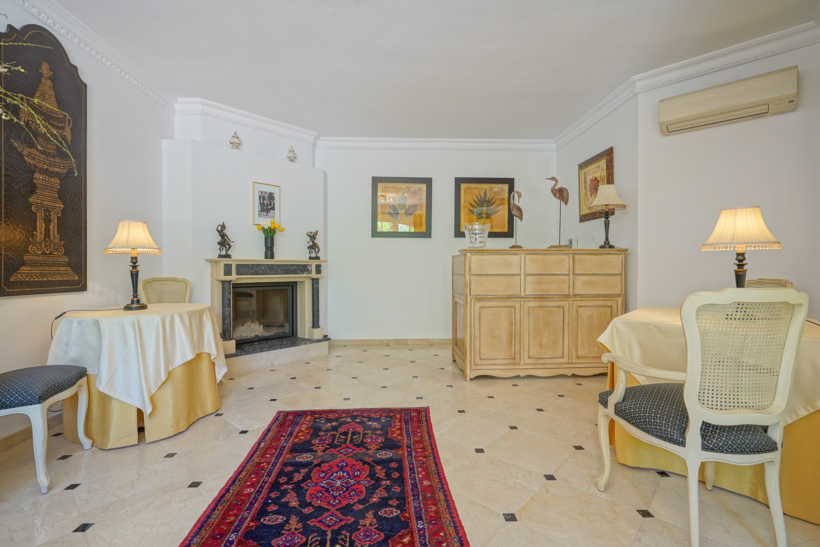 Salon raffiné avec cheminée en marbre, sol en carrelage à cabochons noirs et mobilier classique agrémenté de décorations orientales et moulures.